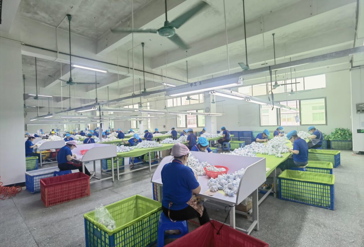 工場の作業台に小型の縫製品を並べて確認する作業風景